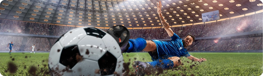 Piłkarz w niebieskim stroju ślizga się po murawie w dynamicznej akcji przy piłce na stadionie.